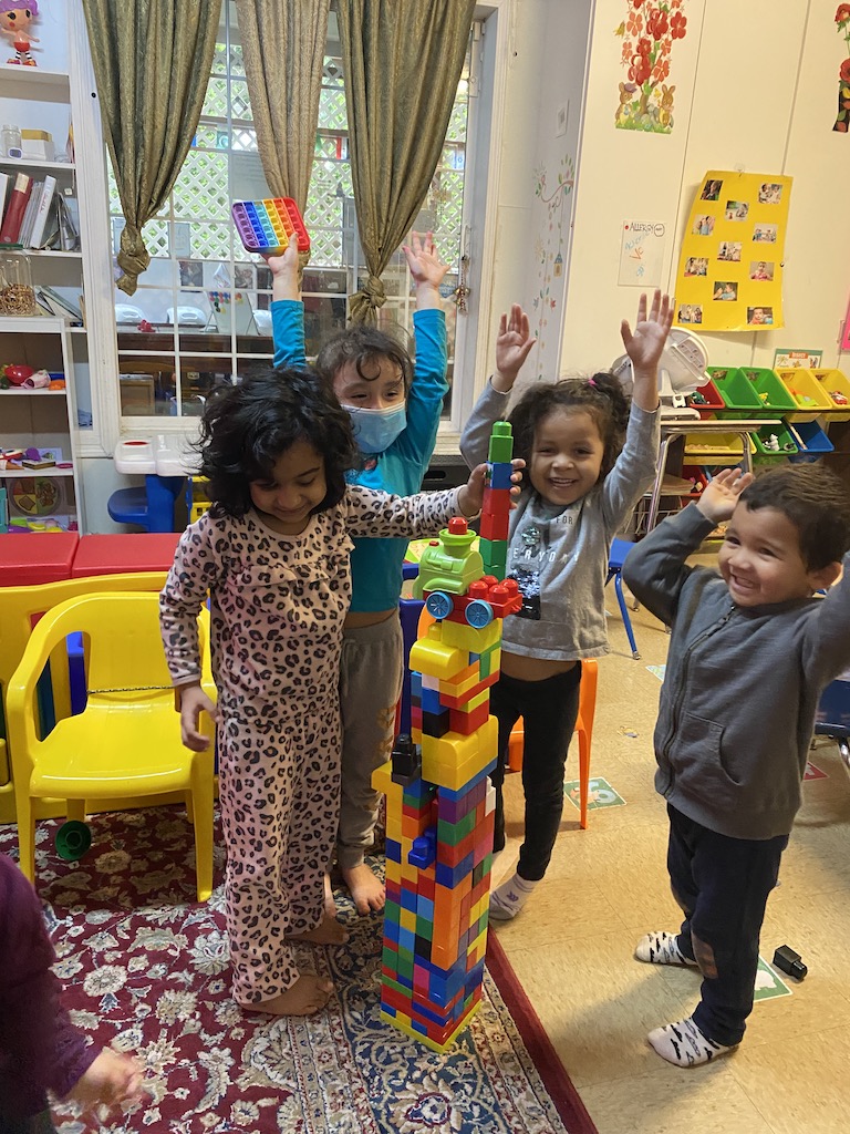Children engaged in play, building structures with colorful blocks in a bright classroom setting.