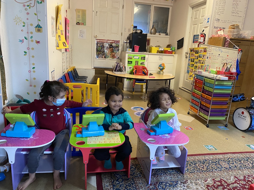 Three children seated in chairs, engaged in a classroom setting, focused on their learning activities.