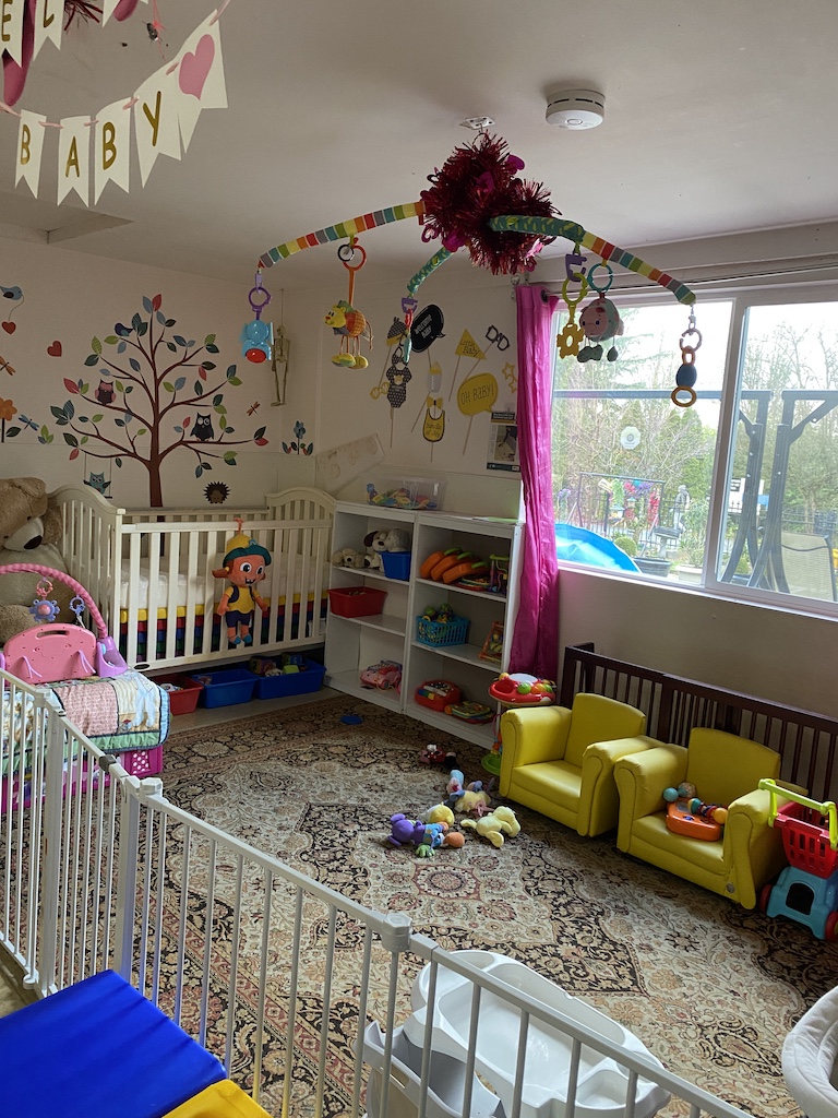 A cozy baby room featuring a crib, a playpen, and a toddler bed, designed for comfort and safety.