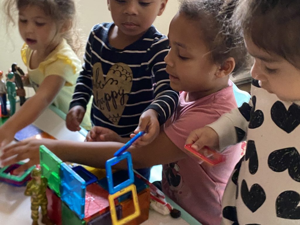 Three children joyfully building with colorful blocks at a table, showcasing creativity and teamwork in play.